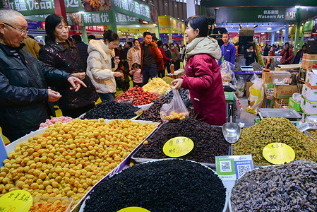 A vendor in a red coat serves customers at a stall selling dried fruits and preserves at the Fuyang Spring Festival shopping fair.