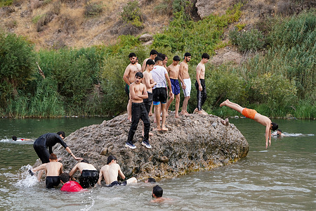 Young men stand on a rock in the Khabur river before jumping into the water in Kurdistan Region. A heat wave is sweeping most cities with temperatures reaching around 50 degrees Celsius.