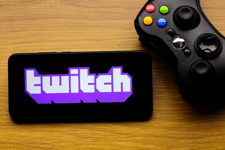 In this photo illustration, the Twitch logo is seen displayed on a smartphone screen next to an Xbox video game controller.
