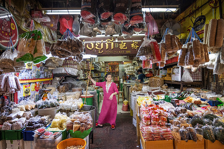 A woman wearing an elegant long pink dress working in a shop in a popular street market in the Chinatown district of Bangkok.