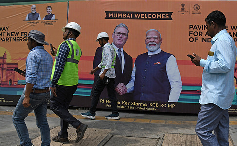 People walk past a poster of Indian Prime Minister Narendra Modi shaking hand with his counterpart, Prime Minister of United Kingdom, Keir Starmer on the streets of Mumbai. The meeting between Indian Prime Minister Narendra Modi and Prime Minister of United Kingdom, Keir Starmer is to boost ties between India and United Kingdom in the areas like trade, defence, security and technology. Prime Minister of United Kingdom along with Indian Prime Minister Narendra Modi visited Global Fintech Fest (GFF) and they gave keynote speeches at the event.