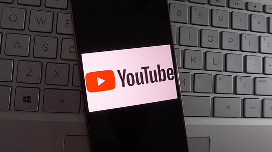 In this photo illustration, Youtube logo is displayed on a smartphone with a laptop keyboard background.