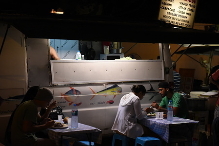 People eating from a Les Roulottes at Vaiete square.
Dozens of food trucks, also known as 'Les Roulottes', congregate every night at Vaiete Square in Tahiti’s capital, Papeete. They serve from: traditional island fare, Poisson cru to cheeseburgers, pizza, and Chinese food. These menus reflect the mashup of cultures that have shaped the cuisine in this island.