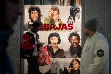 People walk along the main street past a shop window with sale signs. This January 7th, once the Christmas holidays are over the winter sales begin in both large and small shops.