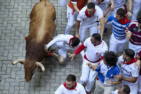 Several runners run in front of the bulls through the streets during the running of the bulls at the San Fermín 2025 festivities. The bulls are from the Jandilla ranch.