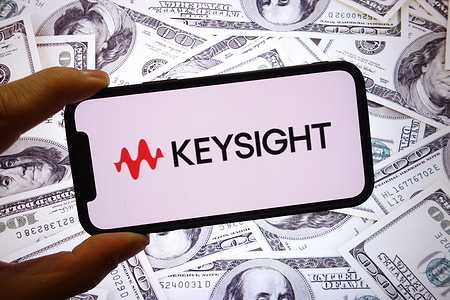 In this photo illustration, the Keysight company logo is seen displayed on a smartphone screen with United States dollar banknotes in the background.