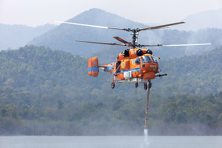 A helicopter performs water pickup operations over a reservoir in Chiang Mai, northern Thailand, as part of aerial firefighting efforts against ongoing wildfires. A KA-32 helicopter from the Department of Disaster Prevention and Mitigation skims the water surface to collect water before heading to fire-affected forest areas amid hazy conditions caused by smoke and rising PM2.5 pollution.