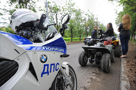A police motorcycle of the Russian DPS (Road Patrol Service) is parked on the roadside as officers inspect teenagers riding quad bikes on a public street during a routine traffic safety check.