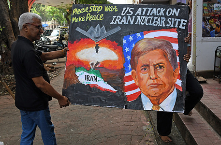 A teacher (L) and a student from the Gurukul School of Art carry back a poster painted with a message urging Israel and Iran to stop the ongoing war between the two nations on the street outside their art school.