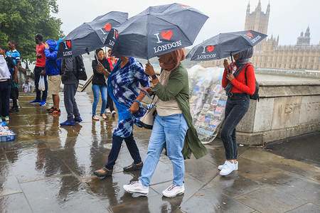 Tourists on Westminster Bridge with souvenir umbrellas during rain showers as a month's rainfall was expected in three hours with the risk of flooding in some areas of the United Kingdom.