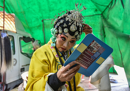 A Chinese opera actor looks into a mirror backstage as he adjusts his costume during a break in an opera performance in rural Fuyang.