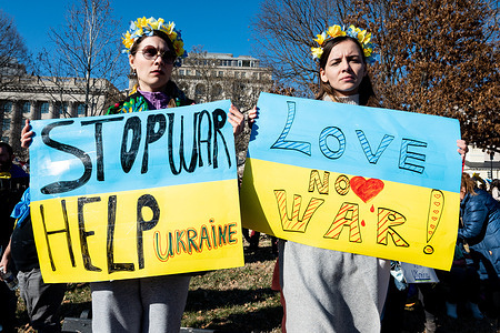 Women hold signs saying "Stop war help Ukraine" and "Love, no war!" at a "Stand With Ukraine" rally.