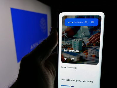 In this photo illustration, a person is holding a smartphone with the web page of energy company Axia Energia (Electrobras) on screen in front of logo.