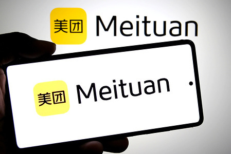 In this photo illustration, the Meituan logo is seen displayed on a smartphone and in the background.