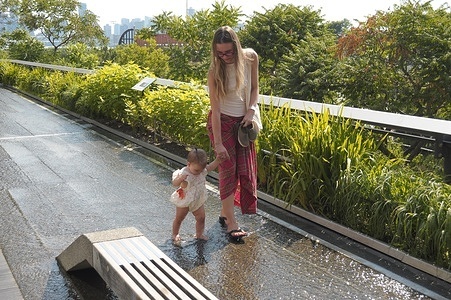 A woman walks with a toddler across a wet surface on the High Line during a summer heat wave in Manhattan. New Yorkers are experiencing high temperatures above 90 degrees Fahrenheit and humid weather. Weather advisories are urging people to stay cool and hydrated.