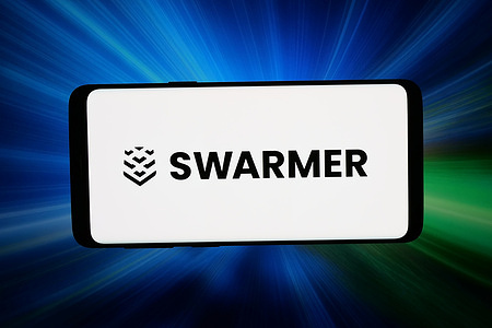 In this photo illustration, the logo of US UAV software company Swarmer Inc. is displayed on a smartphone in front of abstract background on computer screen.
