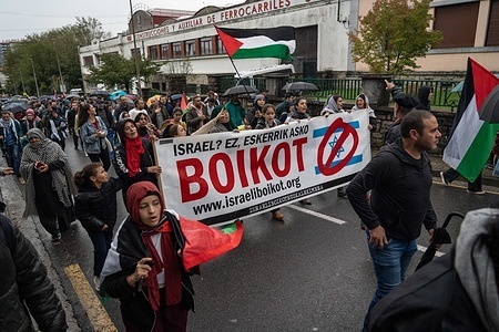 Demonstrators are seen marching while holding a banner during the demonstration. Pro-Palestine demonstrators gathered at Construcciones y Auxiliar de Ferrocarriles (CAF) to protest the company's sale of trains to Israel, urging a boycott of such transactions. They showed solidarity with Palestine amidst the ongoing conflict with Hamas, impacting Gaza, where over 11,000, including children, have died due to continuous Israeli attacks. The demonstration extended from Hendaye in France to Irun, Spain, with participants marching to express their support.