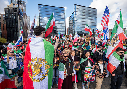 Man draped in Iranian flag films a crowd during the rally. Hundreds of Pro Iranian regime change supporters marched through Manchester City Centre. The demonstration, organized by the members of the 'All Together 4 Iran' group, took place as the Iran-US war entered its fifteenth day. Flags included those of the USA, Israel, the UK and the prerevolutionary flag of Iran. Signs were carried in support of Reza Pahlavi, support of Donald Trump and comparing the deceased Ayatollah Ali Khamenei to Adolf Hitler.