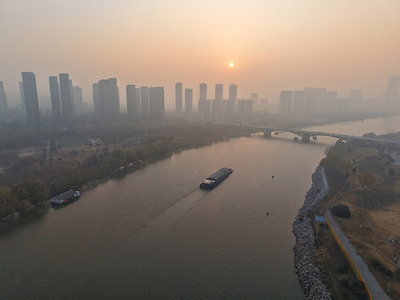 A cargo boat glides on the river as high-rise buildings and a bridge emerge from hazy fog at sunrise. China will grant municipal governments greater autonomy to implement city-specific real estate policies, a move aimed at consolidating the property market's recovery trajectory.