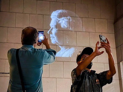 People take pictures of Queen's image projected outside the wall of British Consulate General Hong Kong. Crowds in Hong Kong queued in sweltering heat outside the British Consulate General Hong Kong to pay tribute to Britain’s Queen Elizabeth II on the day of her funeral. People brought flowers and lit candles across the streets.