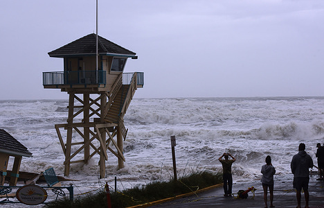 People watch the waves crash near a lifeguard tower in Daytona Beach Shores in Florida, as tropical Storm Nicole approaches the coast of Florida with an expected landfall as a category one hurricane.
