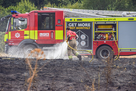A London Fire Brigade firefighter extinguishes a grass fire in a field.