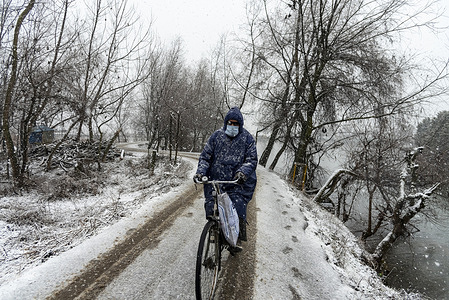 A man looks on as he rides a bicycle along a snow covered road during snowfall. Kashmir received fresh snowfall with higher reaches of the valley receiving moderate to heavy snowfall and light to moderate snowfall in plains, causing disruptive visibility. This impacted flight operations along with the closure of Srinagar-Jammu national highway.