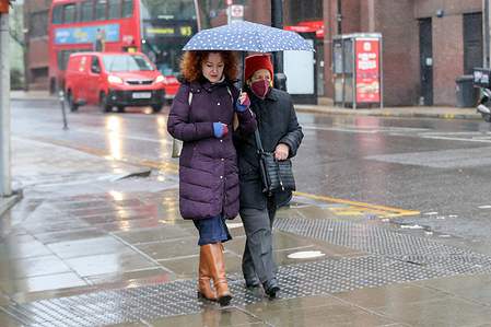 Women shelters under an umbrella during rainfall in London on a wet and windy day in the capital.
