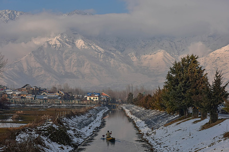 A boatman rows his boat in the back waters of Dal lake with snow covered mountains in the backdrop during a winter day after fresh snowfall in Srinagar.