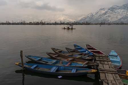 A boatman rows his boat past snow clad mountains during a cloudy day in Srinagar.