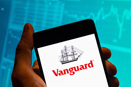 In this photo illustration, the mutual funds and ETFs, brokerage investing services company Vanguard logo is seen displayed on a smartphone with an economic stock exchange index graph in the background.