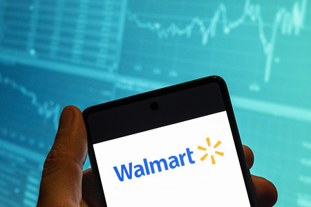In this photo illustration, the American multinational department stores Walmart logo is seen displayed on a smartphone with an economic stock exchange index graph in the background.