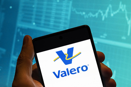 In this photo illustration, the American multinational oil and gas company Valero logo is seen displayed on a smartphone with an economic stock exchange index graph in the background.