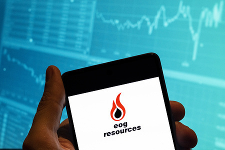 In this photo illustration, the American energy company EOG Resources logo is seen displayed on a smartphone with an economic stock exchange index graph in the background.
