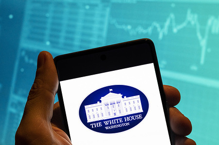 In this photo illustration, the United States official presidency residence, The White House logo is seen displayed on a smartphone with an economic stock exchange index graph in the background.