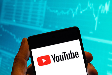 In this photo illustration, the American video-sharing website platform owned by Google, Youtube, logo is seen displayed on a smartphone with an economic stock exchange index graph in the background.