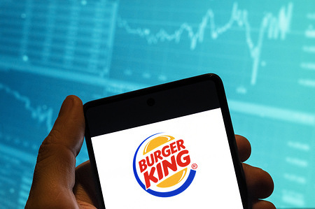 In this photo illustration, the American chain of hamburger fast food restaurants Burger King logo is seen displayed on a smartphone with an economic stock exchange index graph in the background.