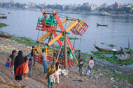 Children are seen playing on the wooden Ferris wheel near the banks of the river Buriganga in Dhaka.