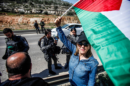Israeli left-wing activist waves a Palestinian flag in front of the Israeli army forces that prevent her from entering the town of Hara to protest against the attacks of Jewish settlers on Palestinian property, near the town of Hawara, south of Nablus, in the occupied West Bank.