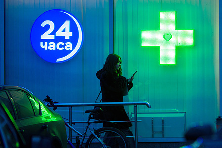 A young lady with a smartphone near the window of a 24-hour pharmacy in Moscow.