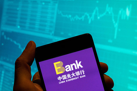 In this photo illustration, the Chinese state-owned banking and financial services enterprise China Everbright logo is seen displayed on a smartphone with an economic stock exchange index graph in the background.