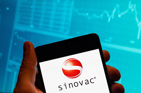In this photo illustration, the Chinese Sinovac vaccine for Covid-19 logo is seen displayed on a smartphone with an economic stock exchange index graph in the background.