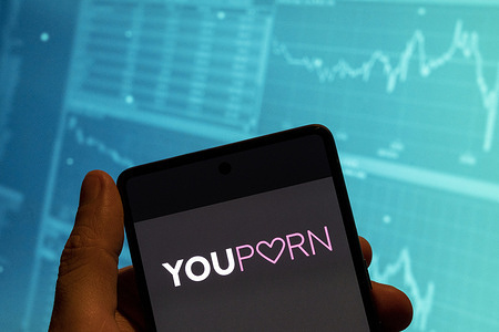 In this photo illustration, the adult pornographic video-sharing website YouPorn logo is seen displayed on a smartphone with an economic stock exchange index graph in the background.