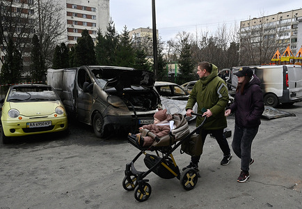 People walk by burnt down cars damaged by a Russian rocket attack next to an apartment building in Kyiv. Russian launched a sustained barrage of missile attacks across Ukraine, damaging both infrastructure and property.