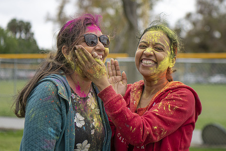Holi Fest participants embrace each other as they rub powder on each others faces in celebration of the holiday. Participants gathered for Holi Fest - Festival of Colors event to celebrate Holi, the official transition from winter to the spring season, hosting live music and providing colored powder to throw at friends and loved ones in the particularly joyful celebration.
