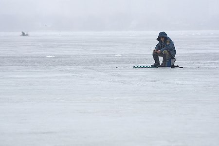 An elderly fisherman in a Rescuer jacket is seen on the thin spring ice of the Voronezh reservoir.