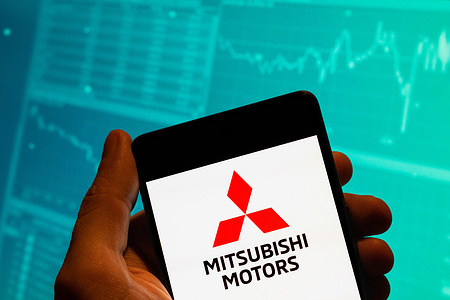 In this photo illustration, the Japanese multinational automotive manufacturer Mitsubishi Motors logo is seen displayed on a smartphone with an economic stock exchange index graph in the background.