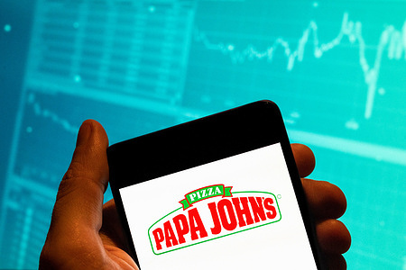 In this photo illustration, the American pizza restaurant franchise Papa John's Pizza logo is seen displayed on a smartphone with an economic stock exchange index graph in the background.