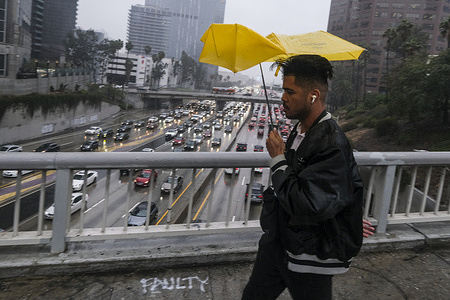 A pedestrian walks with an umbrella as motorists drive through the rain along the Hollywood Freeway near downtown Los Angeles.