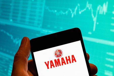 In this photo illustration, the Japanese multinational automobile corporation Yamaha logo is seen displayed on a smartphone with an economic stock exchange index graph in the background.